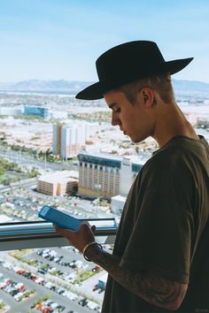 a man in a black hat looking at his book while standing on top of a building