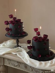 two black cakes with red roses on top and candles in the middle are sitting on a table