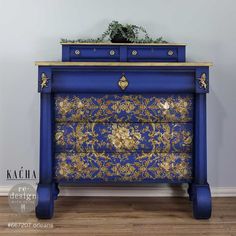 a blue and gold painted dresser with flowers on it's drawers, next to a potted plant