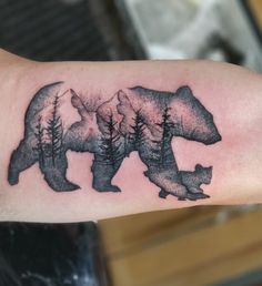 a bear and cub tattoo on the left arm, with trees in the back ground