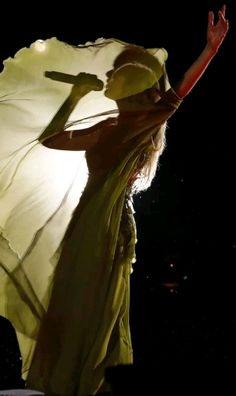 a woman in a white dress is holding her arms out to the side while standing on stage