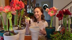 a woman is holding up some flowers in front of potted plants on the table