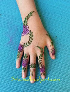 a woman's hand with henna tattoos on her left hand and purple flowers painted on it