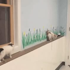 two cats standing on the window sill looking out at the grass and flowers painted on the wall