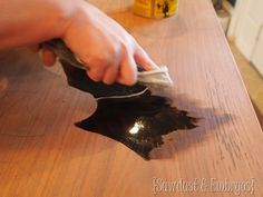 a person wiping up some black paint on a wooden table