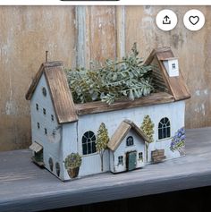 a doll house with plants in it on a table next to a wooden wall and window