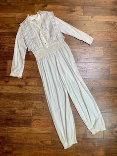 "This super soft white jumpsuit and lace vest set by Miss Dior looks like it belongs on the Alps! It has a stretch waist and buttons halfway up the front. No major flaws, there is some staining on the leg cuffs and a hardly noticeable stain on the front that is covered by the vest. Comes as a set. Bust measures 36\", waist 32\", hips up to 40\", sleeves are 23\" long, and total length is 59\"." Fitted Jumpsuits And Rompers With Lace Trim For Spring, Spring Loungewear Jumpsuits And Rompers With Buttons, White Spring Jumpsuits And Rompers With Buttons, White Buttoned Jumpsuit For Spring, Spring Long Sleeve Jumpsuits And Rompers For Daywear, Long Sleeve Jumpsuits And Rompers For Spring Daywear, White Cotton Jumpsuits And Rompers With Buttons, Cream Fitted Long Sleeve Jumpsuits And Rompers, Cream Fitted Long Sleeve Jumpsuit