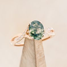 a close up of a ring with a green stone and diamonds on the band, in front of a white background