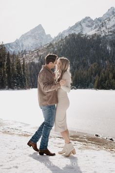 a man and woman standing next to each other on top of snow covered ground with mountains in the background