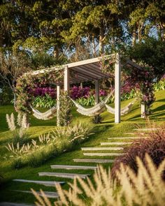 an outdoor garden with flowers and plants on the grass, surrounded by stone steps that lead up to a pergolated area