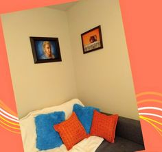 a couch with two orange and blue pillows on top of it next to framed pictures