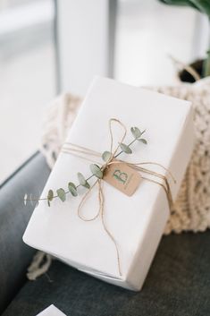 a white present wrapped in twine and tied up with a brown ribbon, sitting on a table next to a potted plant