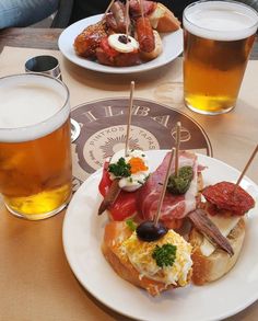 a table topped with plates of food next to glasses of beer on top of it