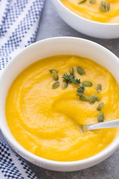 two white bowls filled with yellow soup and topped with pumpkin seeds, sprinkled with green leaves