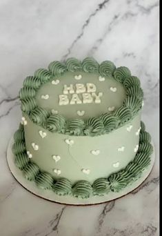 a green and white baby cake on a marble counter top with the words hbd baby written in frosting