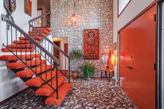 an entry way with stairs and orange pillows on the floor, next to a red door