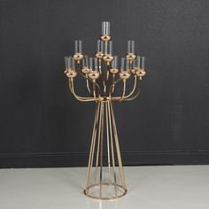 a tall metal and glass candle holder with six candles in it's center, on a white floor