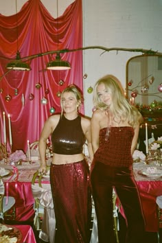 two beautiful women standing next to each other in front of a table with pink cloths