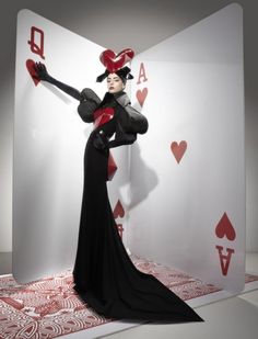 a woman dressed in black and red poses with her arms outstretched while holding playing cards