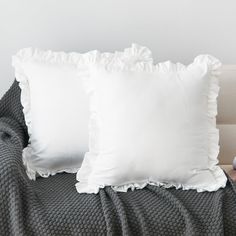 two white pillows sitting on top of a bed next to a gray throw pillow with ruffled edges