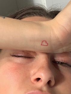 a woman with a heart tattoo on her arm covering her eyes while she is looking at the camera