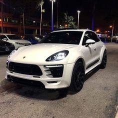 a white porsche cayen is parked in a parking lot at night with its lights on