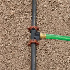 a green and yellow fire hose connected to a pipe on the ground with dirt behind it