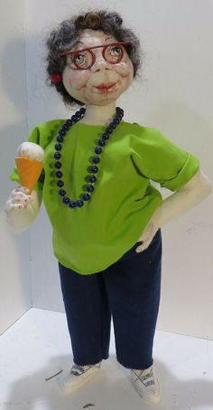 an old doll with glasses and a green shirt holding a drink in one hand and a beaded necklace on the other