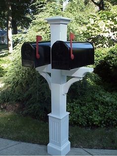 a white post with two black mailboxes on it in front of some bushes