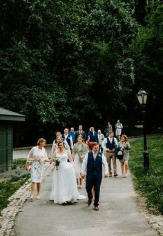 a group of people walking down a road next to each other in front of trees