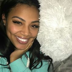 a woman laying on top of a bed next to a white teddy bear and smiling at the camera