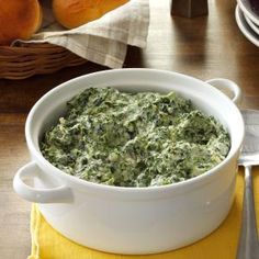 a white bowl filled with spinach on top of a yellow napkin next to silverware