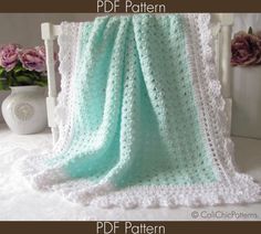 a white crocheted blanket sitting on top of a bed next to a vase with flowers