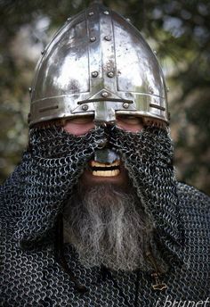 a man with a helmet and chain mail on his face is wearing a metal armor