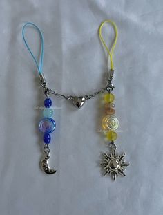 two necklaces with charms attached to them on a white surface, one has a sun and the other is a moon