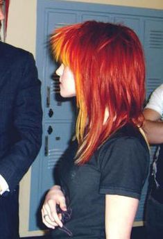 a man in a suit and tie standing next to a red haired woman with bright hair