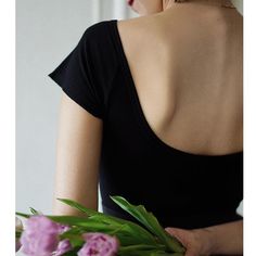 a woman in a black dress is holding a bouquet of pink flowers with her back to the camera