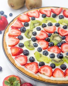 a pie topped with kiwis, strawberries and blueberries on top of a table