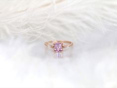 a close up view of a ring with a pink stone in the center and white feathers behind it