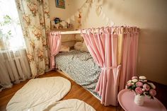 a small child's bed with pink curtains and flowers on the wall next to it