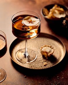 two glasses of alcohol sit on a table next to plates with desserts and drinks