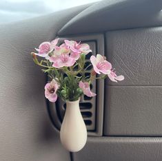 a white vase with pink flowers in it sitting on the dashboard of a car,