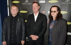 three men standing next to each other in front of a red carpet and black backdrop