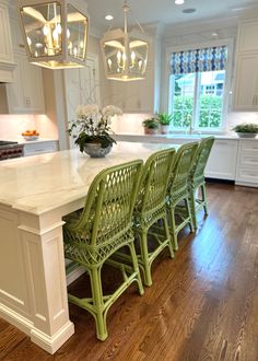 a kitchen with white cabinets and green wicker chairs on the counter top in front of an island