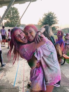 two girls hugging each other in front of a group of people covered in colored paint