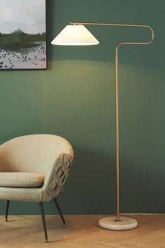 a chair sitting next to a lamp on a wooden floor in front of a green wall