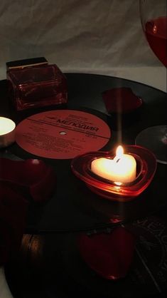 a table topped with candles and records next to a glass of red wine on top of it