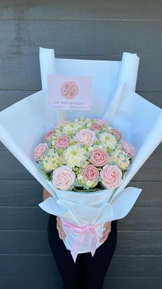 a woman holding a bouquet of flowers in front of a gray wall with a sign on it