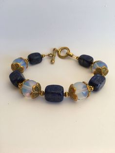 "7.5\"-- 20mm Retangular lapis lazuli gemstone beads and 12mm Opalite Stone beads beautiful statement bracelet, ornate with 15mm brass gold flower caps and a 20mm toggle clasp closure. Hand made jewelry. All purchase will arrive in gifts boxes. Thanks for stopping by!" Blue Moonstone Beaded Bracelets With Gemstone Beads, Handmade Blue Moonstone Beaded Bracelets, Handmade Blue Moonstone Bracelets, Opalite Bracelet, Chakra Stones Jewelry, Bracelet Weaving, Stone Bead Jewelry, Beautiful Beaded Jewelry, Girl Bracelet