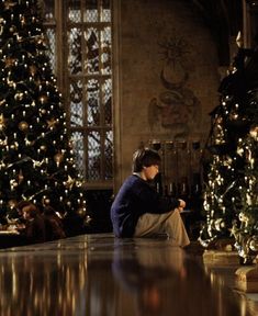 a woman sitting on the floor in front of christmas trees with lights all around her